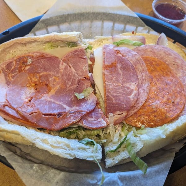 A large Rinaldi's Italian Deli sub sandwich, cut in half, filled with various meats, cheese, and lettuce.