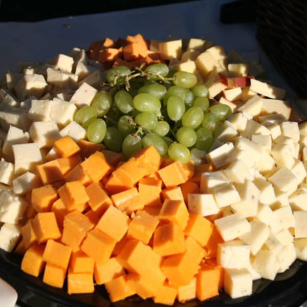 A platter of cubed cheeses in white and orange, with a cluster of green grapes in the center.