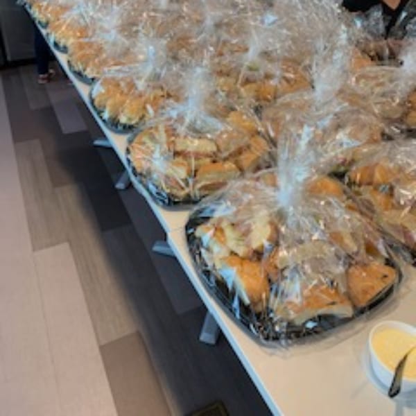 Numerous trays of individually wrapped Rinaldi's Italian Deli sandwiches are arranged on a table.