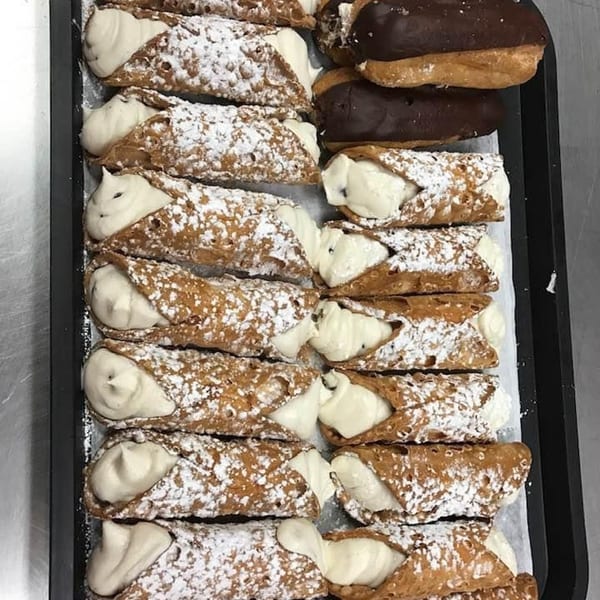 A tray of Rinaldi's Italian Deli cannolis and chocolate eclairs dusted with powdered sugar.