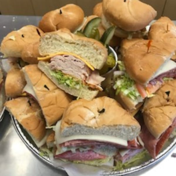 A catering platter overflowing with various Rinaldi's Italian Deli sandwiches, some with pickles.