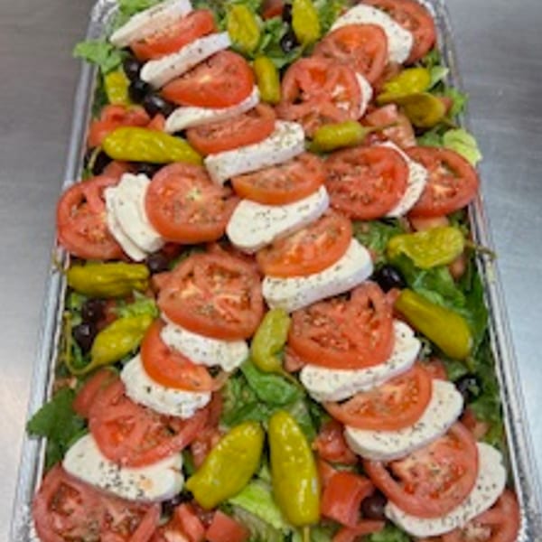 A large catering tray of Rinaldi's Italian Deli salad with tomatoes, mozzarella, and peppers.