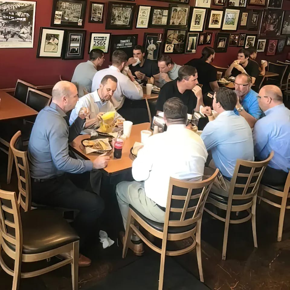 Customers enjoying sandwiches and drinks at Rinaldi's Italian Deli, surrounded by framed photos.
